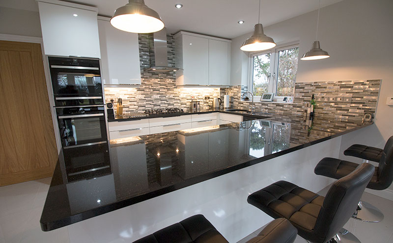 This modern kitchen near Swanage in Dorset features stone and glass mosaic splash backs with high gloss white porcelain floor tiles