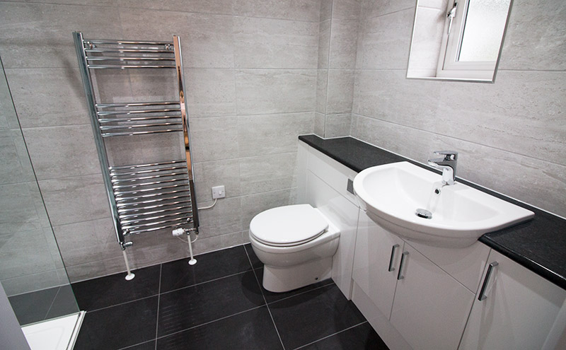 A luxury master ensuite bathroom by UK Tiles Direct featuring gloss black large format porcelain floor tiles with white stone effect wall tiles