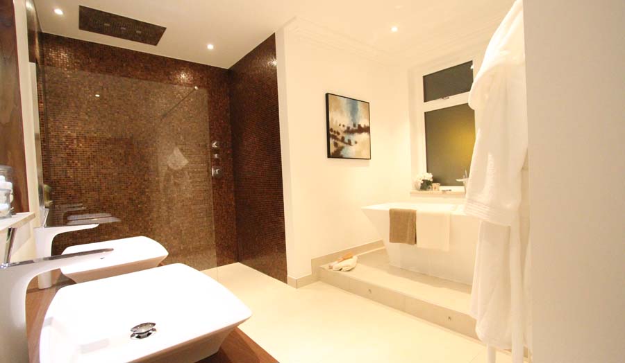 A luxury bathroom and wetroom with rust coloured mosaic and contrasting large porcelain floor tiles by Room H2O