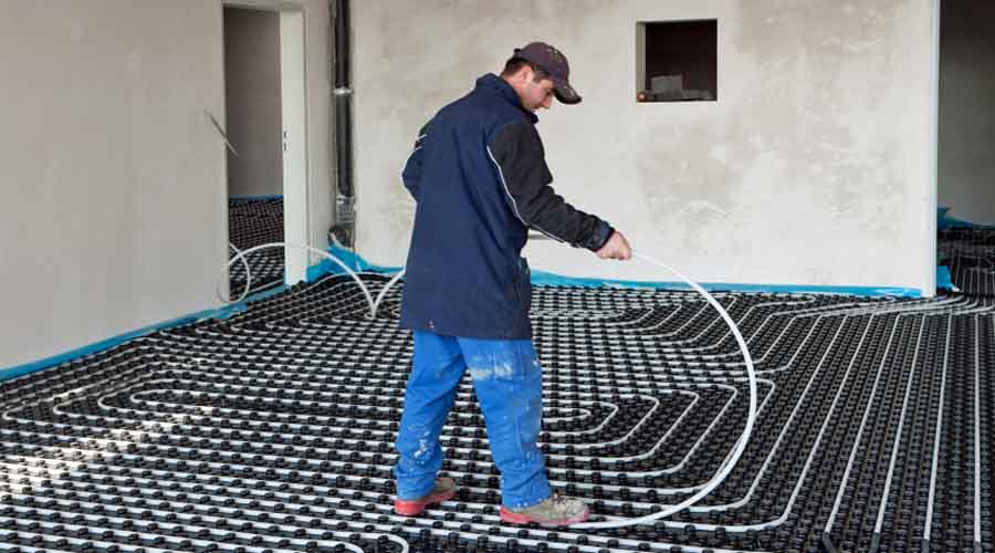 A heating engineer installing wet undefloor heating pipes into a large luxury new build house
